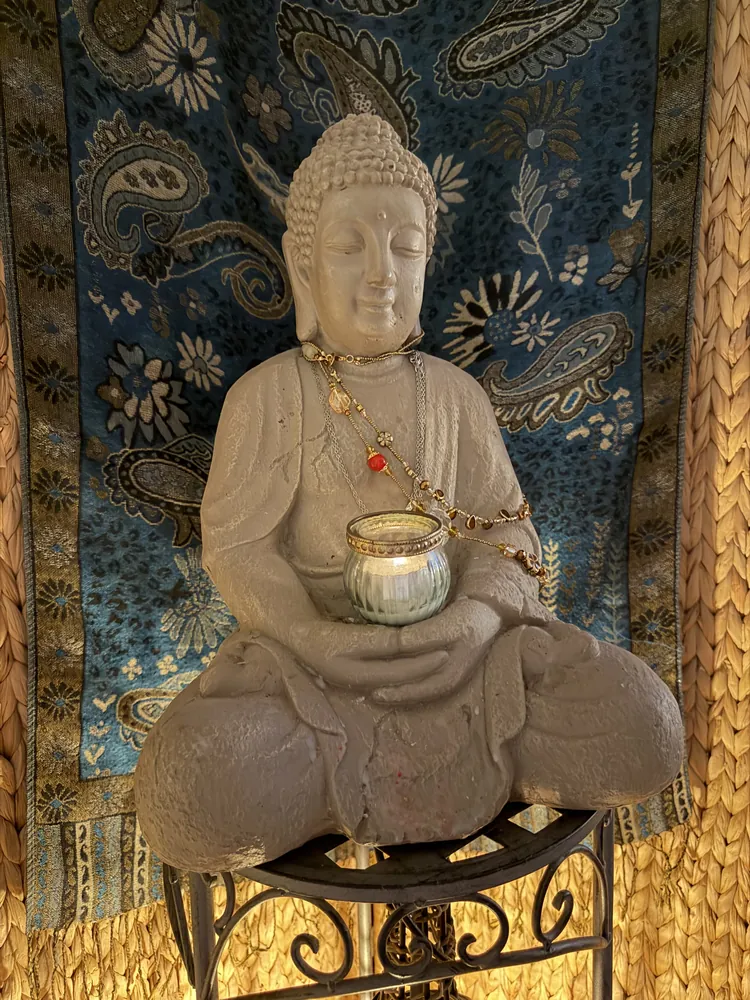 Weiße Buddha-Figur mit Teelicht vor einem Paisley-Tuch